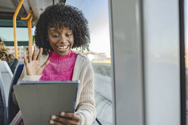 Happy woman waving on video call through tablet PC in tram - JCCMF09086