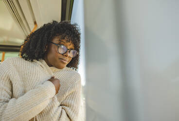 Lächelnde Frau mit Brille schaut durch ein Fenster in der Straßenbahn - JCCMF09087
