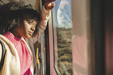 Nachdenkliche junge Frau schaut durch ein Fenster in der Straßenbahn - JCCMF09088