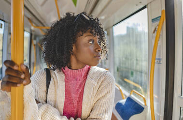 Junge Frau mit lockigem Haar in der Straßenbahn stehend - JCCMF09089