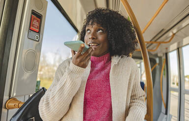 Junge Frau mit lockigem Haar, die in der Straßenbahn mit ihrem Smartphone telefoniert - JCCMF09092
