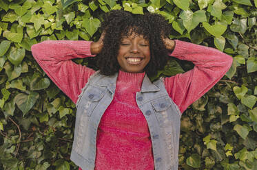 Happy woman with eyes closed standing in front of plants - JCCMF09096