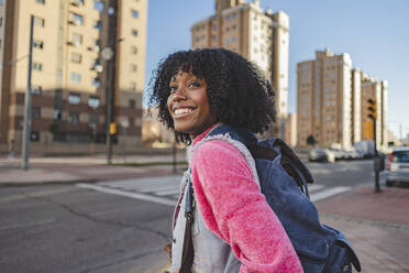 Happy young woman with backpack standing on footpath - JCCMF09099