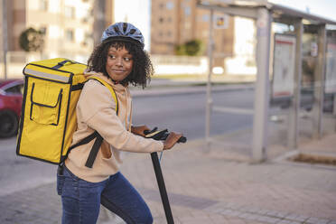 Lächelnde Zustellerin mit Elektro-Scooter auf dem Gehweg - JCCMF09113