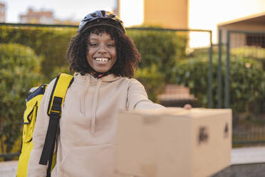 Glückliche Zustellerin mit Fahrradhelm bei der Paketübergabe - JCCMF09116