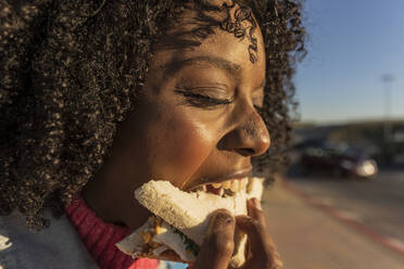 Junge Frau mit lockigem Haar isst Sandwich - JCCMF09127