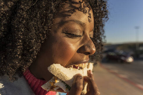 Junge Frau mit lockigem Haar isst Sandwich - JCCMF09127