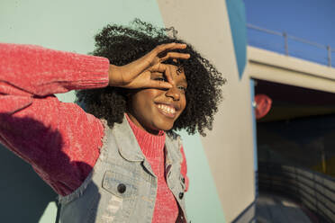 Happy young woman gesturing OK sign in front of wall - JCCMF09139