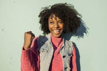 Happy young woman cheering in front of green wall - JCCMF09140