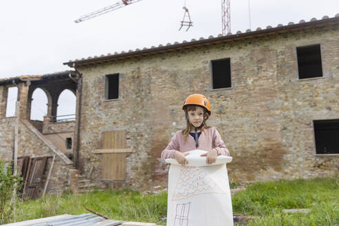 Mädchen mit Schutzhelm steht mit Zeichnung vor einem Haus - EIF04201
