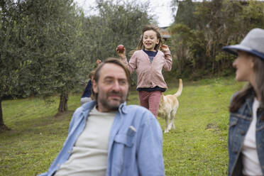 Man and woman sitting on grass with daughter running in background - EIF04211
