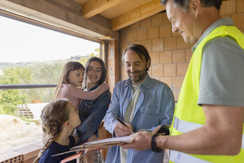 Älterer Mann mit Familie bei der Unterzeichnung eines Dokuments auf einer Baustelle - EIF04256