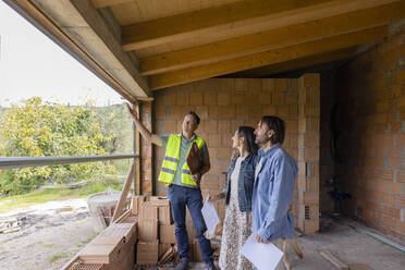 Glücklicher Bauunternehmer im Gespräch mit einem reifen Paar auf der Baustelle - EIF04259