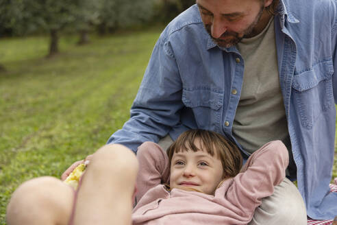 Lächelndes Mädchen entspannt sich mit ihrem Vater auf einem Feld sitzend - EIF04274