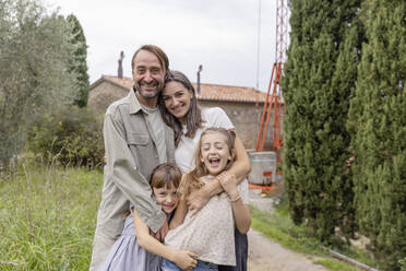 Happy mature woman and man standing with daughters in front of house - EIF04334