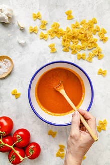 Hand of woman preparing tomato sauce amidst farfalle - FLMF00893