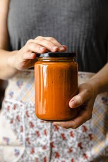 Hands of mature woman holding homemade tomato sauce jar - FLMF00901