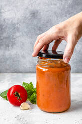 Hand einer Frau beim Öffnen des Deckels eines Tomatensoßenglases - FLMF00903