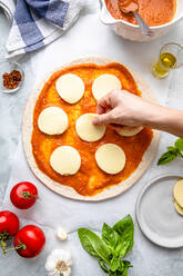 Hand einer Frau, die eine Pizza auf einem Tisch zubereitet - FLMF00909