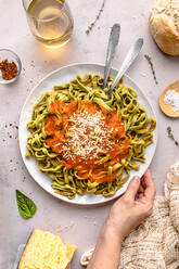 Hand of mature woman with spinach tagliatelle and tomato sauce served in plate on table - FLMF00920