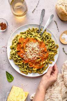 Hand einer reifen Frau mit Spinat-Tagliatelle und Tomatensauce in einem Teller auf dem Tisch - FLMF00920