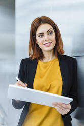 Smiling businesswoman using tablet PC leaning on wall - DIGF19721