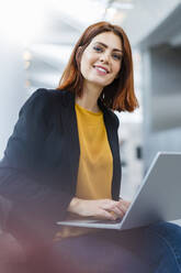 Smiling businesswoman with laptop sitting down - DIGF19727