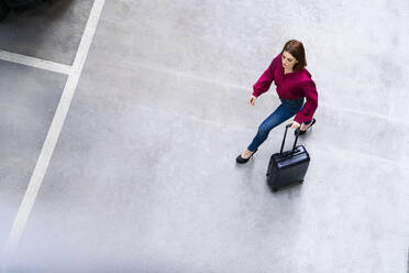 Businesswoman with wheeled luggage walking at parking lot - DIGF19763