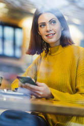 Smiling businesswoman holding mobile phone in cafe - DIGF19769