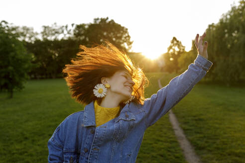 Carefree woman with hand raised enjoying in park at sunset - VIVF00334