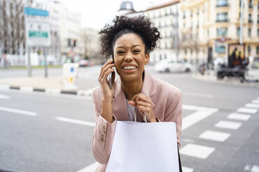 Glückliche Geschäftsfrau mit Einkaufstüten, die mit einem Smartphone telefoniert - JJF00019
