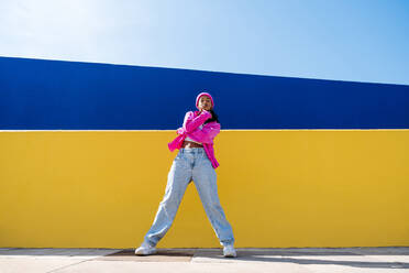 Young woman standing in front of yellow wall on sunny day - OIPF03028