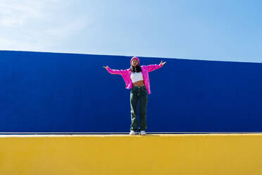 Woman with arms outstretched dancing in front of blue wall - OIPF03045