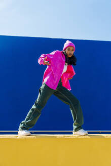 Junge Frau in rosa Jacke macht Hip-Hop-Tanz an der Wand - OIPF03050