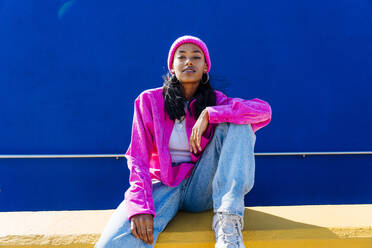 Junge Frau in rosa Jacke an der Wand sitzend - OIPF03062