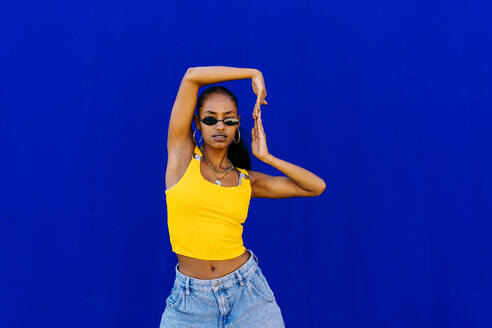 Young woman wearing sunglasses dancing in front of blue wall - OIPF03075