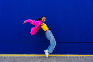 Happy woman dancing on tiptoe by blue wall - OIPF03084