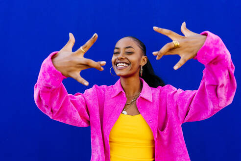 Happy young woman crossing fingers in front of blue wall - OIPF03089