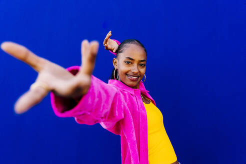 Smiling young woman dancing in front of blue wall - OIPF03093