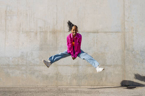 Fröhliche Tänzerin springt vor der Wand an einem sonnigen Tag - OIPF03097