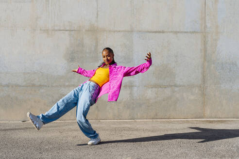 Lächelnde junge Frau tanzt vor einer Wand - OIPF03109
