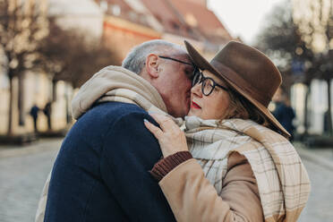 Senior man kissing woman wearing hat and scarf - VSNF00382