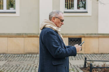 Älterer Mann mit Smartphone vor einem Gebäude - VSNF00384