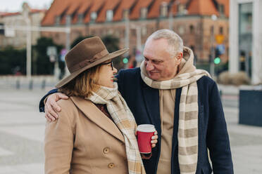Lächelnder älterer Mann umarmt Frau mit Einwegbecher - VSNF00407