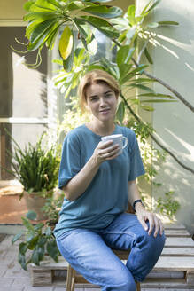 Smiling woman with coffee cup sitting on bench - SVKF01170