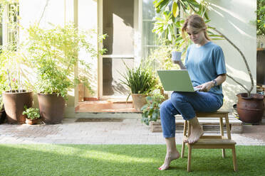 Freiberufler mit Kaffeetasse und Laptop im Garten sitzend - SVKF01173