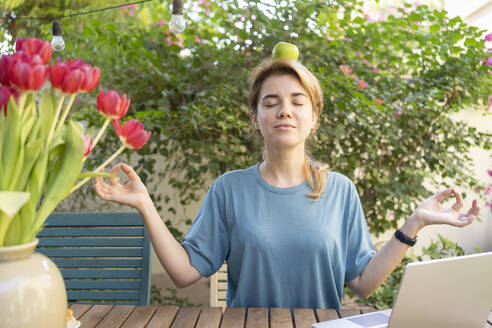 Freelancer balancing green apple on head sitting in garden - SVKF01178