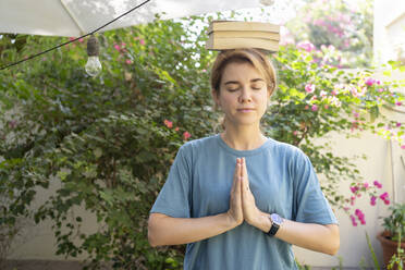 Woman with eyes closed and hands clasped balancing books on head - SVKF01186