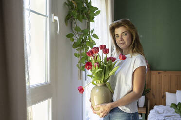Smiling woman standing with bouquet of tulips at home - SVKF01202