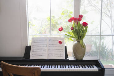 Piano with bouquet of tulips and music sheets in front of window at home - SVKF01204